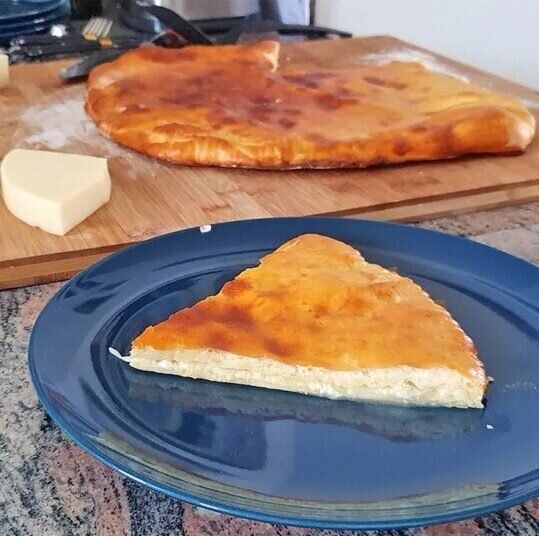 Запечённый сырный хлеб с золотистой корочкой, нарезанный на куски, на деревянной доске