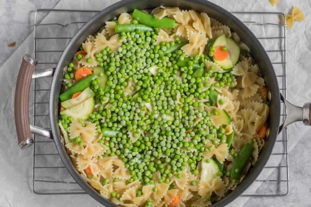 Готовый овощной макаронный микс в сковороде, показывающий яркие кусочки цукини, моркови и зеленого горошка