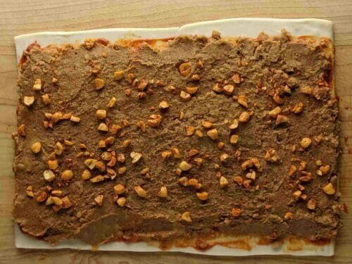 Готовый рулет самоса, нарезанный кольцами, поданный на белой тарелке с листиками кинзы и ломтиками огурца